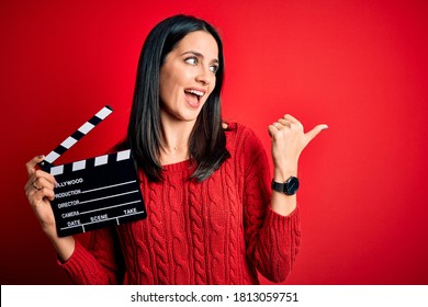Sutradara muda wanita dengan mata biru membuat film sambil memegang papan berdinding merah sambil menunjuk dan menunjukkan jempol ke samping dengan wajah bahagia tersenyum