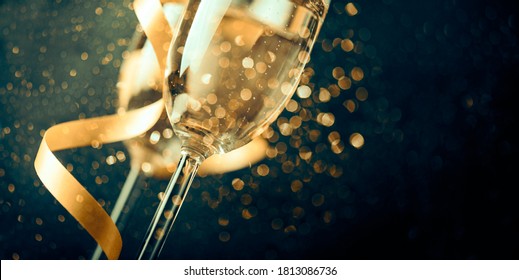 Two champagne glasses with golden ribbon and gold glitter splash bokeh on dark background. Luxury restaurant dinner celebration. Classy christmas and new year holiday panoramic design banner.