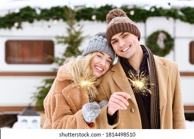 Smiling Romantic Couple In Knitted Hats Posing With Sparklers At Winter Camping, Holding Bengal Lights In Hands And Looking To Camera, Celebrating Christmas Holidays Together At Campsite, Copy Space