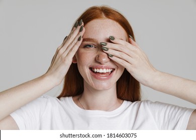 Image of happy ginger girl smiling and covering her eyes isolated over gray background