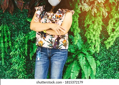 植物の背景を持つ女性のジーンズのベルトループにぶら下がっているコロナウイルス(Covid-19)を殺すミニポータブルアルコールジェルボトル. ニューノーマルなライフスタイル。ヘルスケアのコンセプト。アルコールジェルの選択と集中
