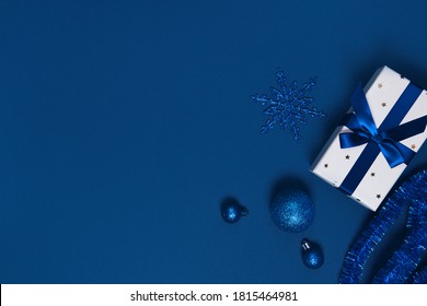 Present box wrapped with a ribbon, decorative balls and snowflake on colorful paper background. Christmas gift. Holiday concept. Image is with copy space. Flat lay. Top view
