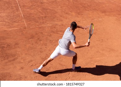 Professionele tennisspeler voert forehand hit op gravel tennisbaan. Jonge mannelijke atleet met tennisracket in actie. Tennissport voor junioren. Achteraanzicht, schaduw, kopieer ruimte