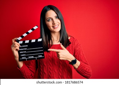 Sutradara muda wanita dengan mata biru membuat film sambil memegang papan berdinding merah dengan sangat gembira sambil menunjuk dengan tangan dan jari