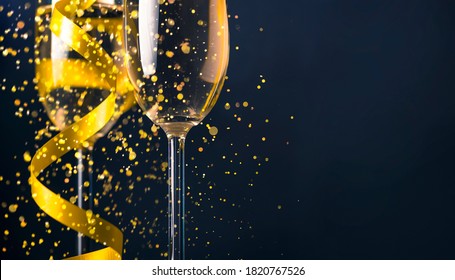 两杯香槟酒配上金色丝带和金色闪光，在深色背景上溅起散景。豪华餐厅晚宴庆典。优雅的圣诞节和新年假期全景设计横幅。