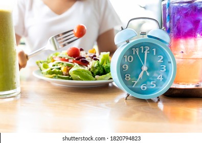 Selective focus of blue clock which woman make a Intermittent fasting with a Healthy food of salad .Healthy lifestyle Concept.