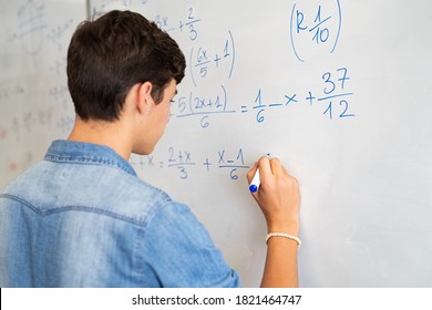 教室のホワイトボードで数学の問題を解く高校生の後ろ姿。マーカーを使用してホワイト ボードに数学のソリューションを書く若い男。授業中に数学表現を解く大学の男。
