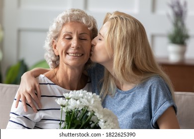 ¡Te amo tanto mi querida! Cariñosa hija milenaria saludando a una madre anciana mayor feliz con el día de la madre, abuela feliz recibiendo un beso tierno y flores con los ojos cerrados de un nieto adulto