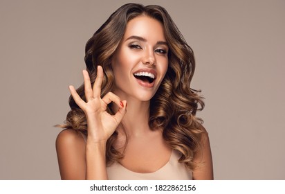 Happy  girl with curly hair   smiling and showing OK sign . Presenting your product. Expressive facial expressions