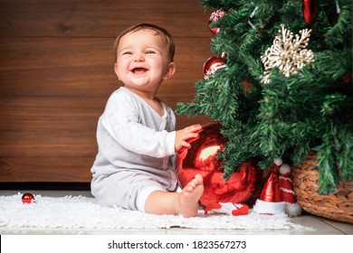 クリスマス ツリーとかわいい子。モミの木のそばに座って、クリスマスの飾りを持って、笑っている幸せな赤ちゃん