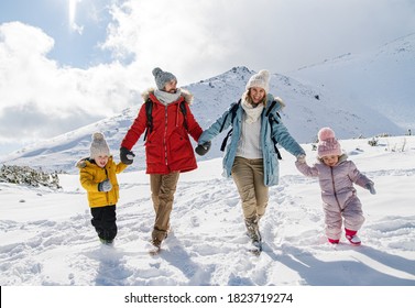 Padre y madre con dos niños pequeños en la naturaleza invernal, caminando en la nieve.