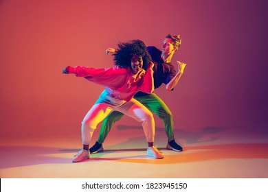 Stijlvolle man en vrouw hiphop dansen in lichte kleding op groene achtergrond in de danszaal in neonlicht. Jeugdcultuur, hiphop, beweging, stijl en mode, actie. Modieus portret.