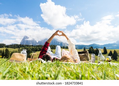 Pareja romántica enamorada haciendo picnic visitando montañas alpes. Novio y novia disfrutando del amor haciendo forma de corazón con las manos al aire libre.