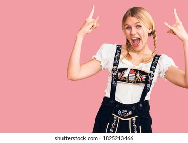 Young beautiful blonde woman wearing oktoberfest dress shouting with crazy expression doing rock symbol with hands up. music star. heavy music concept. 