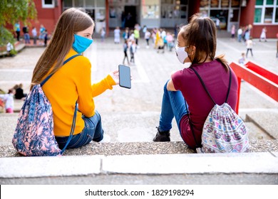 学校の前で電話を使用しているガール フレンド。学校の休み時間に校庭でデバイスの画面を見ている 2 人の 10 代の少女