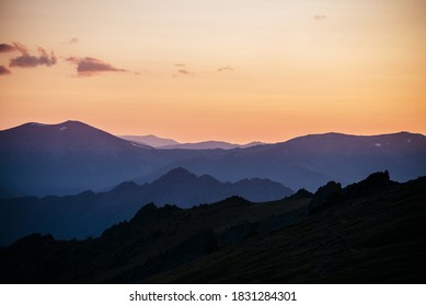 Warmer Farbverlauf des Morgenhimmels über Schichten von Berg- und Felssilhouetten. Lebendige Alpenlandschaft mit dunklen Rockies und orangefarbenem Sonnenaufgangshimmel. Minimalistische Hochlandlandschaft mit Silhouette der Rocky Mountains
