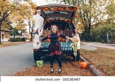 Trick or trunk. Kid child celebrating traditional October holiday Halloween in trunk of car. Cute happy girl throwing leaves in air outdoor. Social distance and safe alternative celebration.