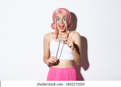 Retrato de chica atractiva con peluca rosa y maquillaje brillante, vestida como un hada para la fiesta de Halloween, sosteniendo la varita mágica y sonriendo