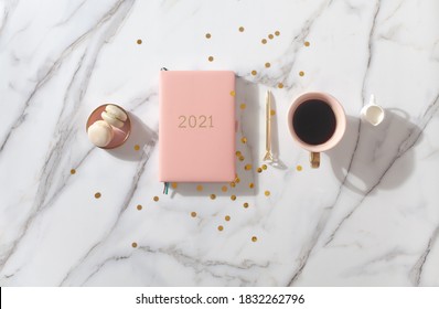 Roze koraalkleurig dagboek voor het jaar 2021, pen, koffie latte, macaron koekje en stro geweven placemat op witte marmeren achtergrond. Nieuwjaar planning concept. Minimalistische werkplek. Kopieer ruimte.