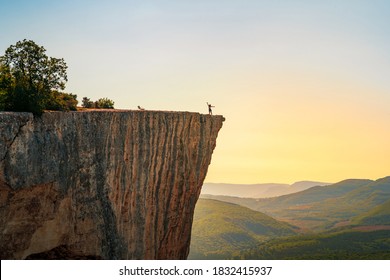 Een kleine figuur van een vrouwelijke toerist met open armen, staande op de rand van een klif in de zomerbergen. Het concept van een kleine man in het midden van een krachtige natuur.