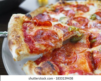 Zoumaachen Vue vun 1/4 engem Véierel Slice vun traditionell authentesch italienesch dënn knusprech Krust Diavola Pizza dropgesat mat roude Ronn dënn geschnidden wierzegen Salami, Wierfel Jalapeno gréng Peffer, Mozzarella Kéis