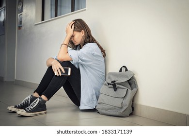 頭を抱えた大学キャンパスの床に座ってスマートフォンを持っている動揺して落ち込んでいる女の子。高校の床に座ってうつ病に苦しんでいる大学の悲しい学生。孤独ないじめられたティーン。