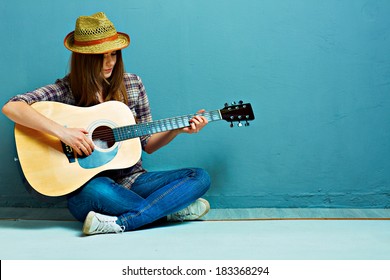 床に座ってティーンエイ ジャーの女の子のギター プレイ。青の背景。カントリー スタイル。