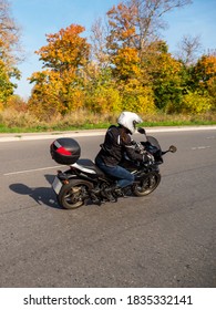 Motorcyklist i bevægelse. Kvindelig biker på en sort motorcykel i trafikken på en landlig efterårsvej.