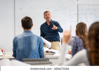 Professor pointing at college student with hand raised in classroom. Student raising a hand with a question for the teacher. Lecturer teaching in class while girl have a question to do during a lesson