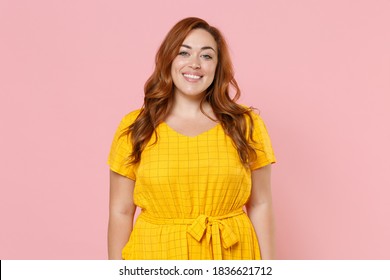 Lächelnde schöne attraktive junge Rothaarige plus Größenkörper positive mollige übergewichtige Frau im gelben Freizeitkleid, das die schauende Kamera lokalisiert auf pastellrosa Farbwandhintergrund-Studioporträt aufwirft