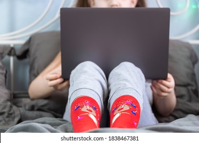 Girl with gray laptop sitting in bedroom in funny winter socks. Cozy holiday