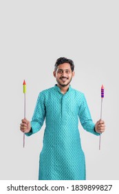 Diwali festival concept, Young Indian man in ethnic wear and holding Glossy exploding Rockets in hand on white background