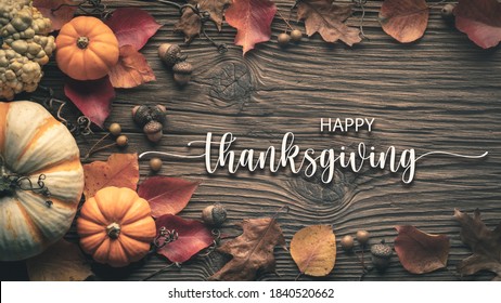 "Happy Thanksgiving"-Nachricht auf rustikalem Erntetischhintergrund, verziert mit Kürbissen, Eicheln und Blättern