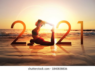 Gelukkig nieuwjaarskaart 2021. Silhouet van gezond meisje dat Yoga One Legged Pigeon doet pose op tropisch strand met zonsondergang hemelachtergrond, vrouw die yoga beoefent als onderdeel van het nummer 2021-teken.