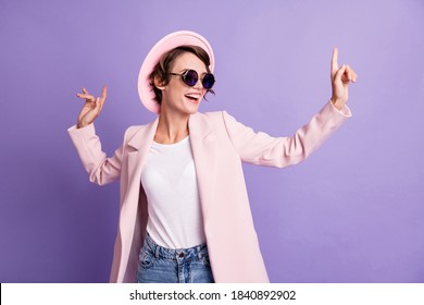 Foto af begejstret dansedisko hit ung brunette kvinde bære kasket briller frakke isoleret på lilla farve baggrund