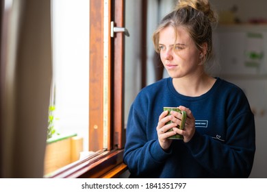 Young blonde blue-eyed girl drinking tea looking out the window