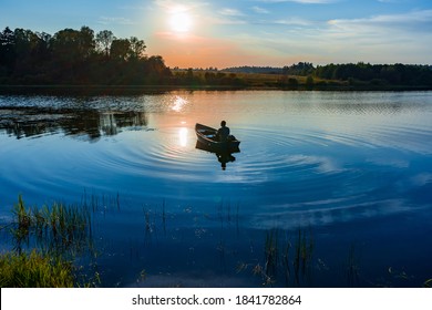 釣り竿を手にした 60 歳の白人男性が、夕暮れ時にモーター付きのボートで湖で釣りをしている