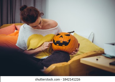 Beautiful caucasian woman making Halloween decoration, holding big pumpkin with painted evil face on