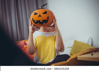 Caucasian female holding big Halloween pumpkin with painted evil face in front of her head