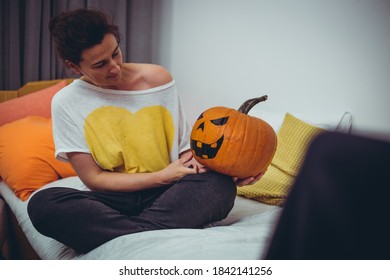 Beautiful caucasian woman making Halloween decoration, holding big pumpkin with painted face on
