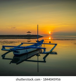 Seascape. Fisherman boat jukung. Sunrise landscape. Gazebos on an artificial island in the ocean. Water reflection. Sun on horizon. Slow shutter speed. Soft focus. Sanur beach, Bali, Indonesia.