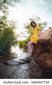 A woman in a yellow jumpsuit stands in the river among large stones.