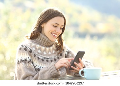 Happy woman wearing jersey using smart phone at breakfast in the mountain in winter