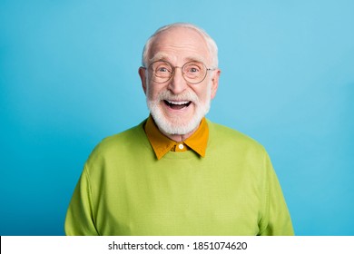 Foto van gepensioneerde oude man met open mond glanzende glimlach opgewonden draag een bril groene trui geïsoleerde blauwe kleur achtergrond
