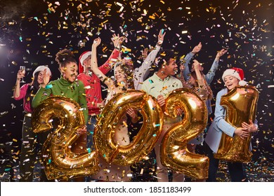 大晦日を祝い、2021年の数字の形で金色のホイル風船を持ち、踊る若い幸せな多民族の人々のグループ