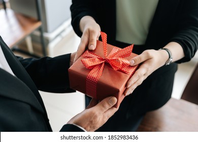 Tampilan close-up dari tangan wanita tak dikenal memberikan kotak hadiah merah diikat ke busur diserahkan kepada pria. Pemberian hadiah saat Natal, Tahun Baru dan Selamat Ulang Tahun di kantor.