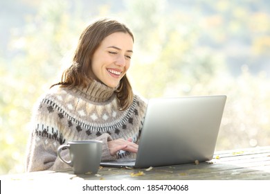 Happy woman using laptop sitting on a table in the mountain in autumn