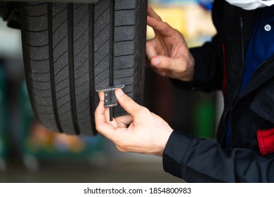 Comprobación mecánica comprobando la profundidad de la banda de rodadura del neumático de coche. Mantenimiento de automóviles y concepto de garaje de servicio automático.