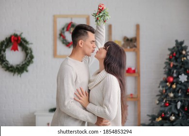 Pasangan muda berciuman di bawah cabang mistletoe di rumah pada malam Natal