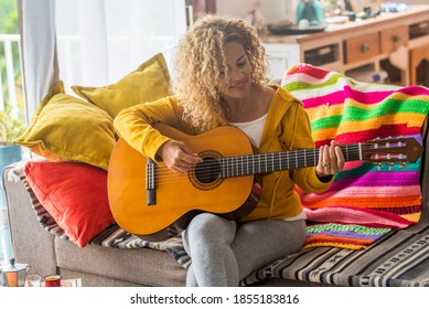 Mooie vrouw van middelbare leeftijd gitaar spelen thuis - muziekles en zanger zittend op de bank - mensen spelen instrument en genieten van liedjes en vrijetijdsbesteding binnen